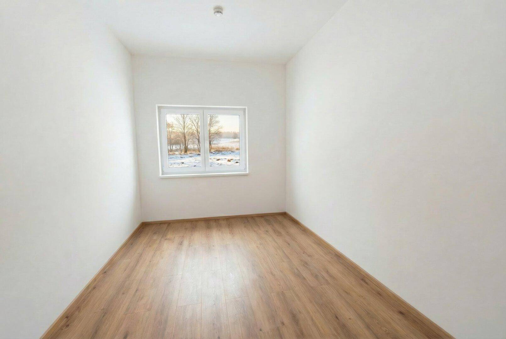 Leeres Zimmer mit Holzboden, weißen Wänden und Fenster mit Blick auf die verschneite Natur.