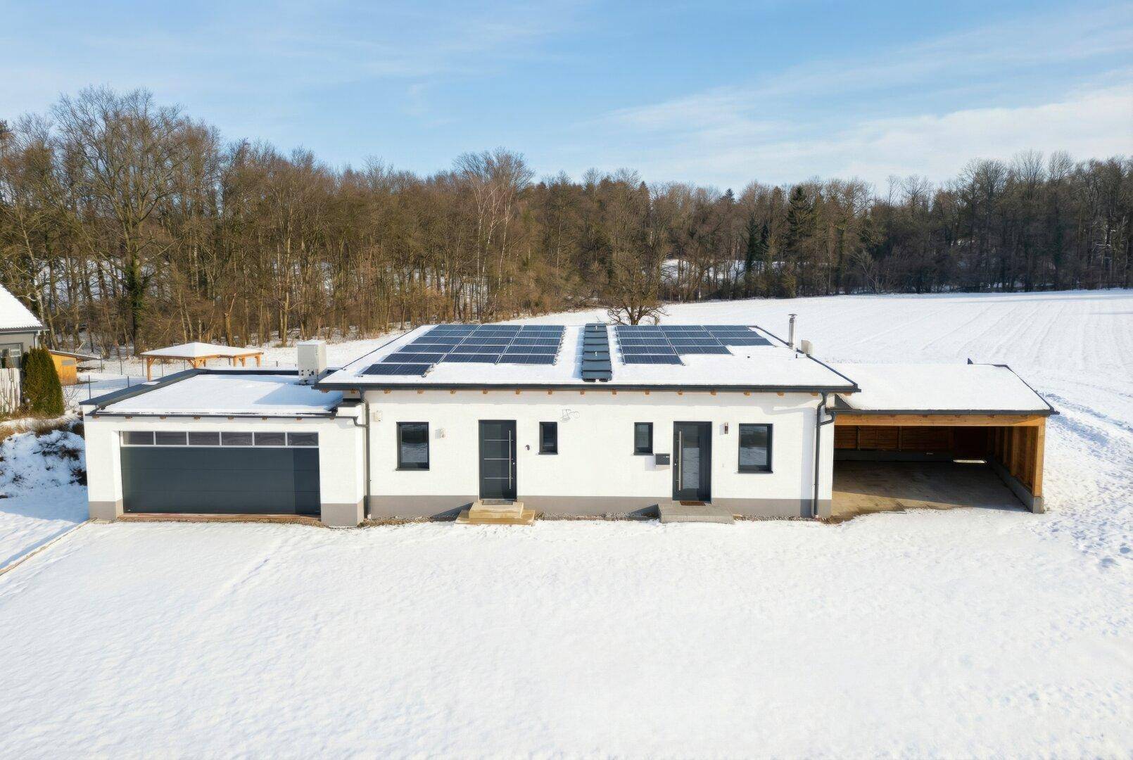 Modernes Einfamilienhaus mit Photovoltaikanlage auf dem Dach, umgeben von Schnee und Natur.
