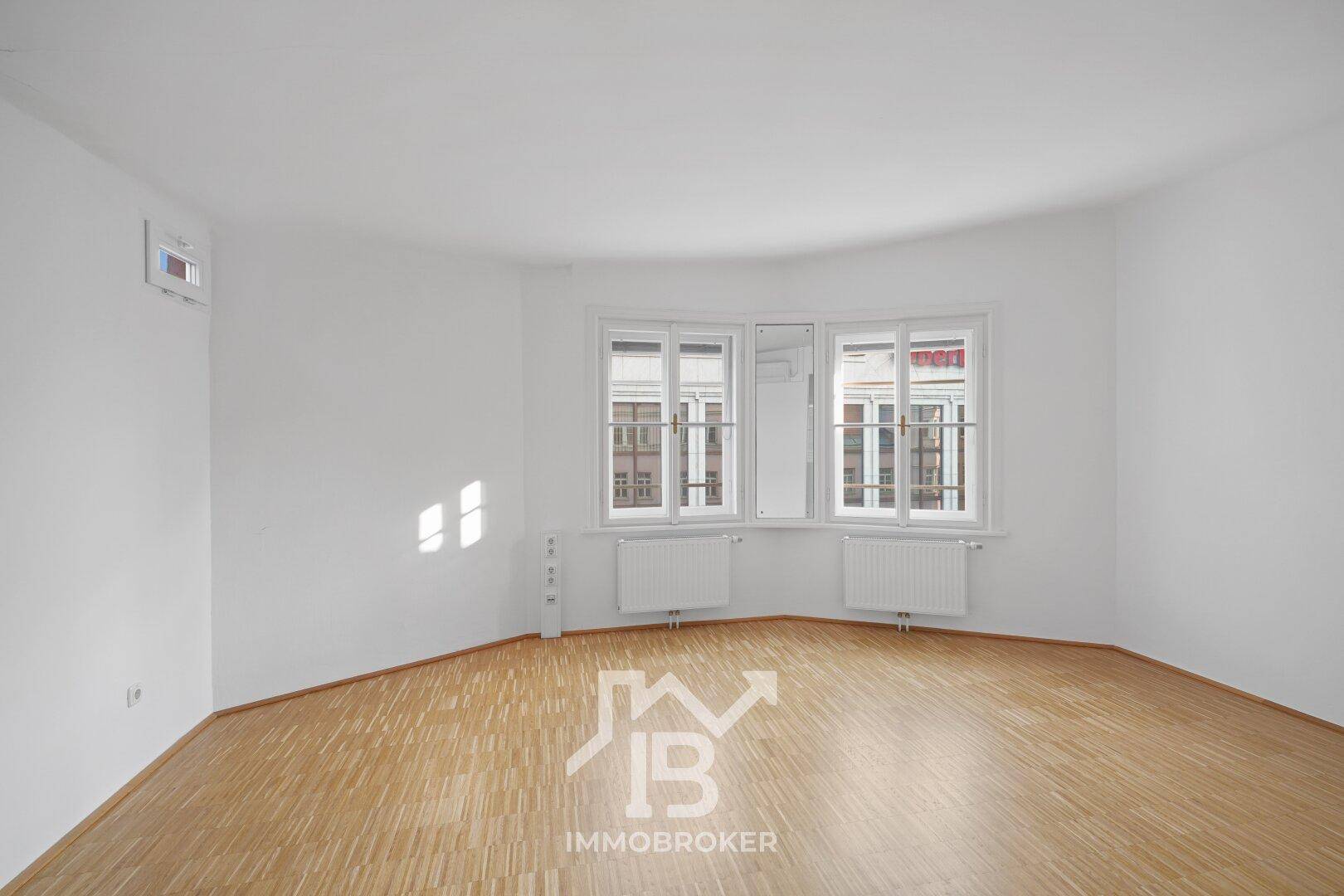 Geräumiger Raum mit Erkerfenster, Parkettboden und Heizkörpern, bietet eine helle und einladende Atmosphäre.