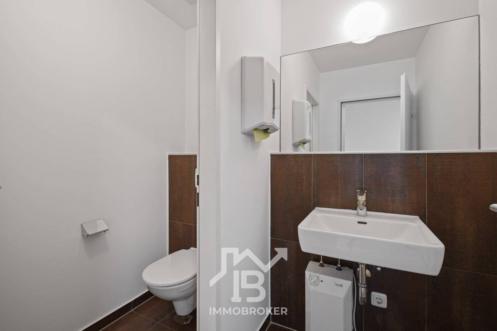 Modernes Badezimmer mit Toilette, Waschbecken und großem Spiegel, ausgestattet mit braunen Fliesen.