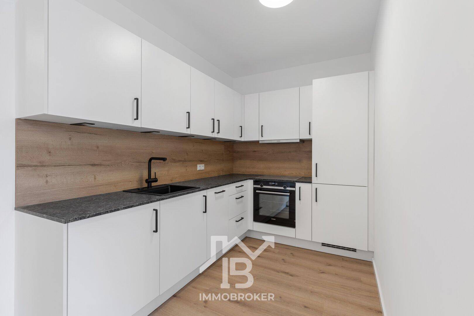 Moderne Einbauküche mit weißen Schränken, dunkler Arbeitsplatte und integriertem Backofen.