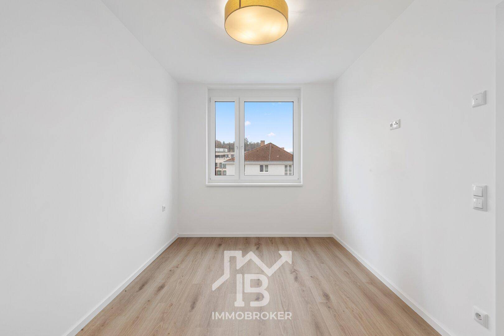 Helles Zimmer mit Parkettboden und großem Fenster, ideal als Schlaf- oder Arbeitszimmer.