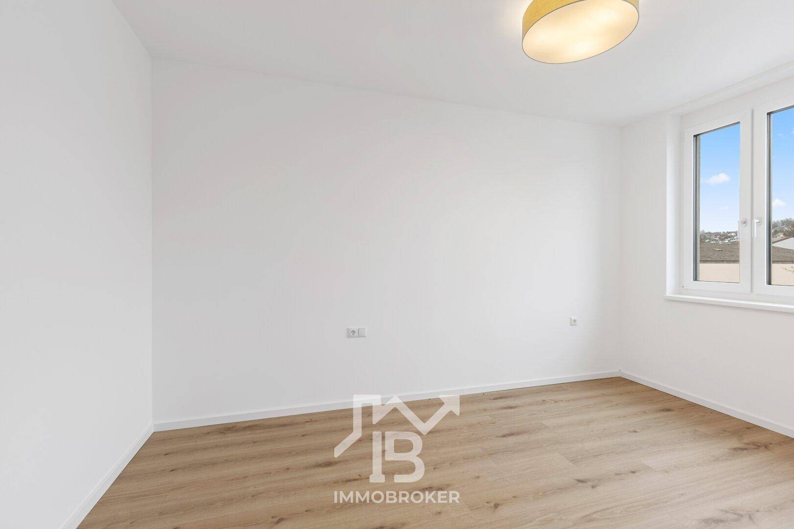 Leeres Zimmer mit weiß gestrichenen Wänden und hellem Parkettboden.