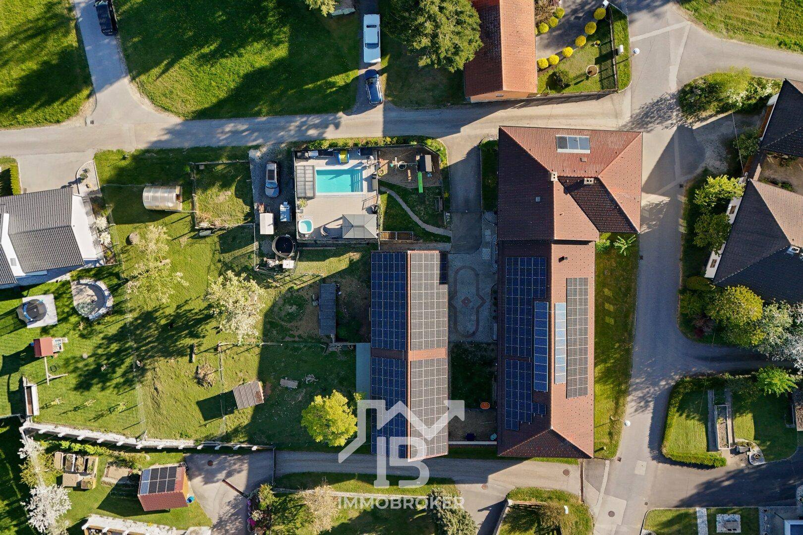 Luftaufnahme eines Wohngebiets mit Häusern, Gärten, Solaranlagen und einem Swimmingpool.