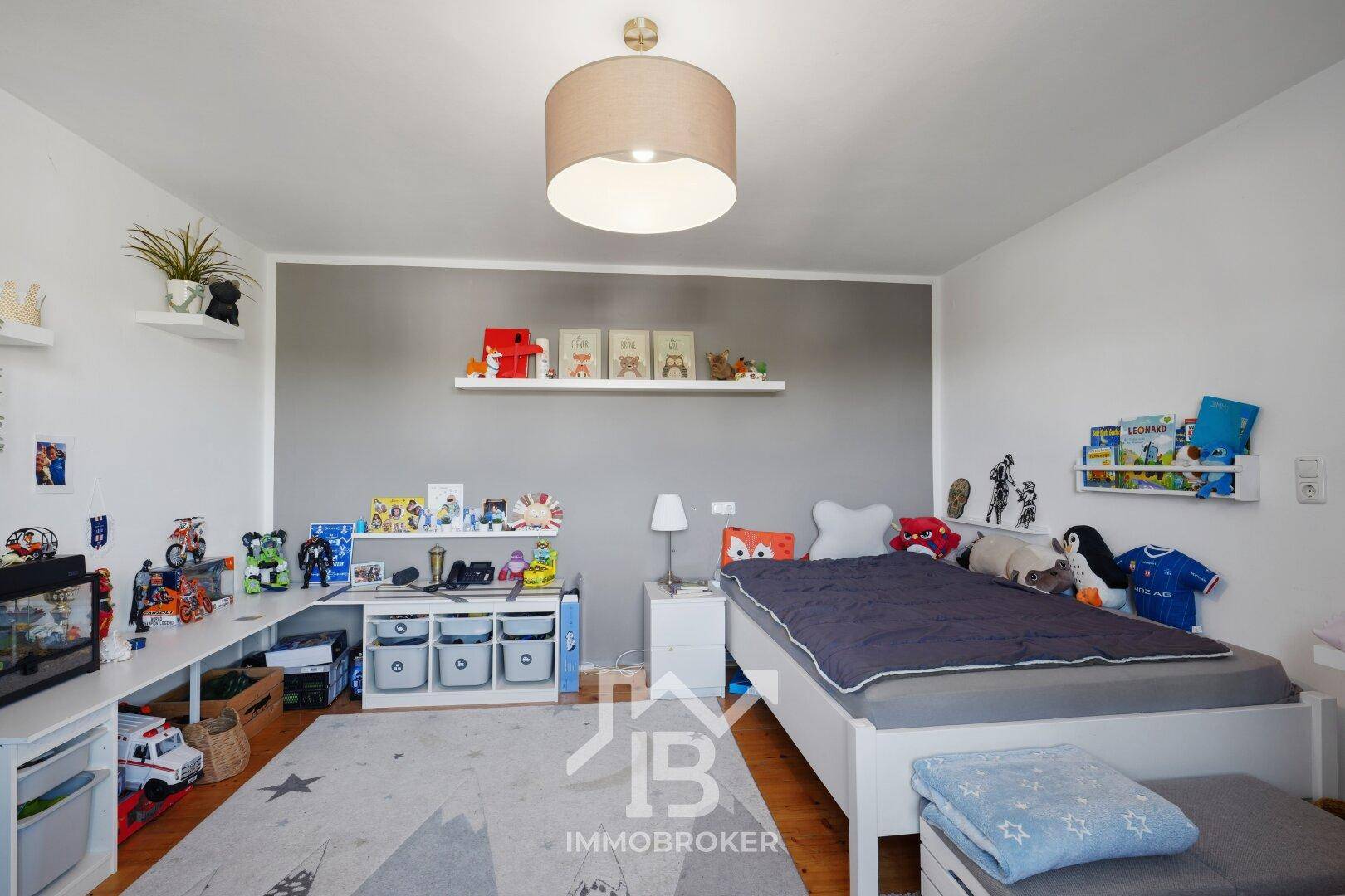 Helles Kinderzimmer mit Einzelbett, Schreibtisch und Spielzeugregalen, freundlich gestaltet.