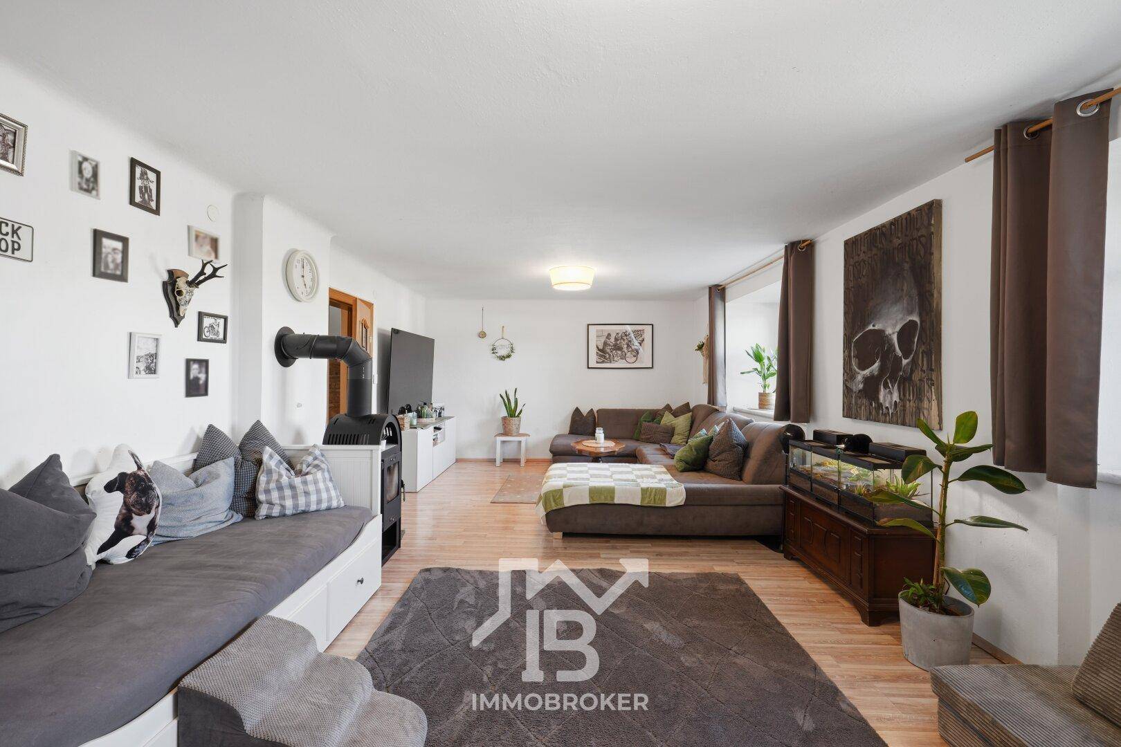 Geräumiges Wohnzimmer mit Holzboden, großem Ecksofa und Kaminofen, hell und gemütlich eingerichtet.