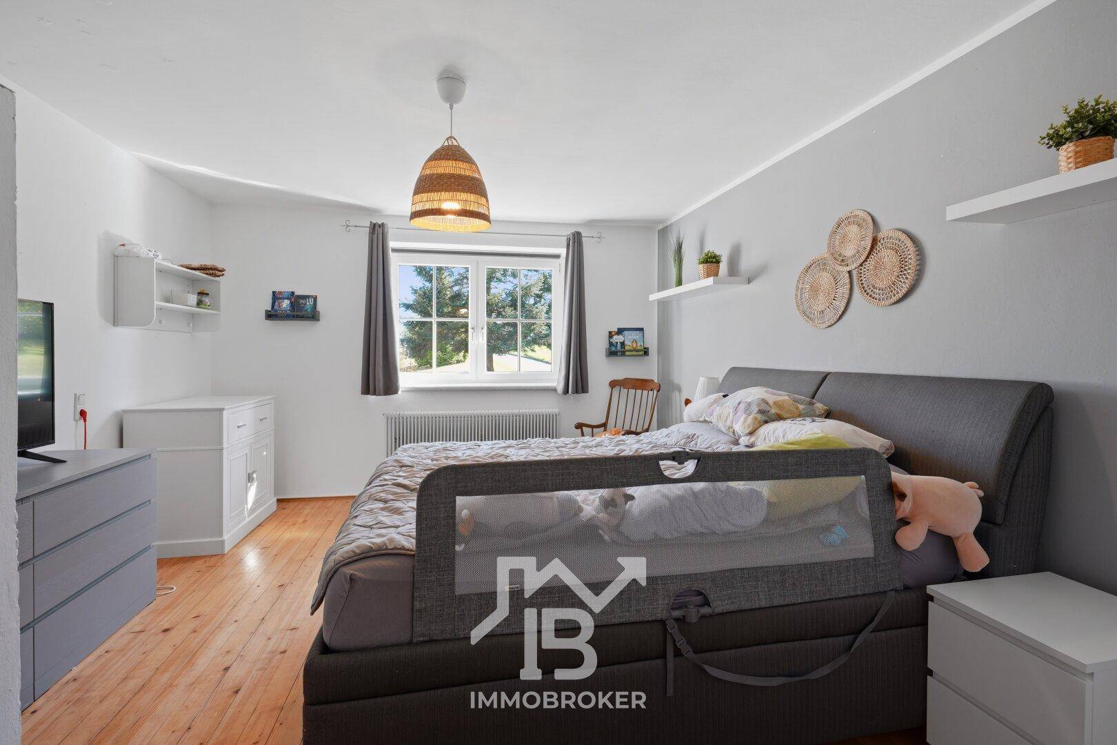 Gemütliches Schlafzimmer mit Doppelbett, Holzboden und Fenster mit Blick ins Grüne.