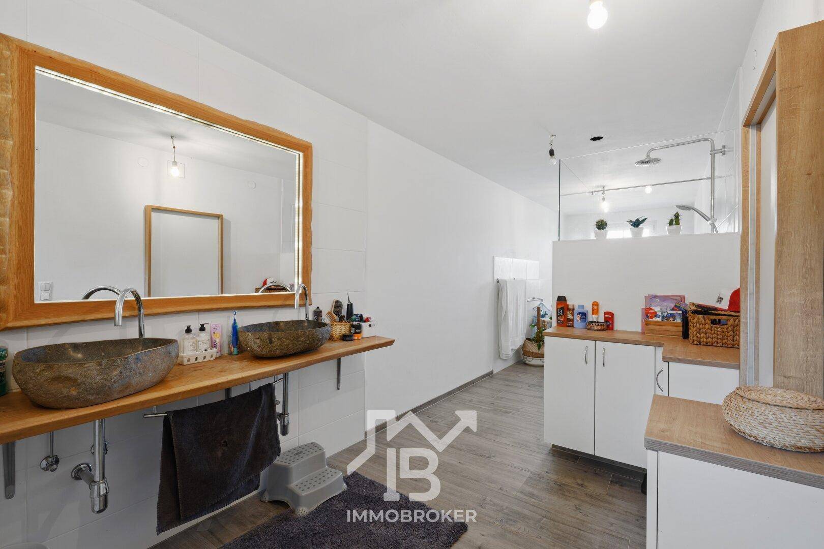Geräumiges Badezimmer mit Doppelwaschbecken aus Stein, großem Spiegel und begehbarer Dusche.