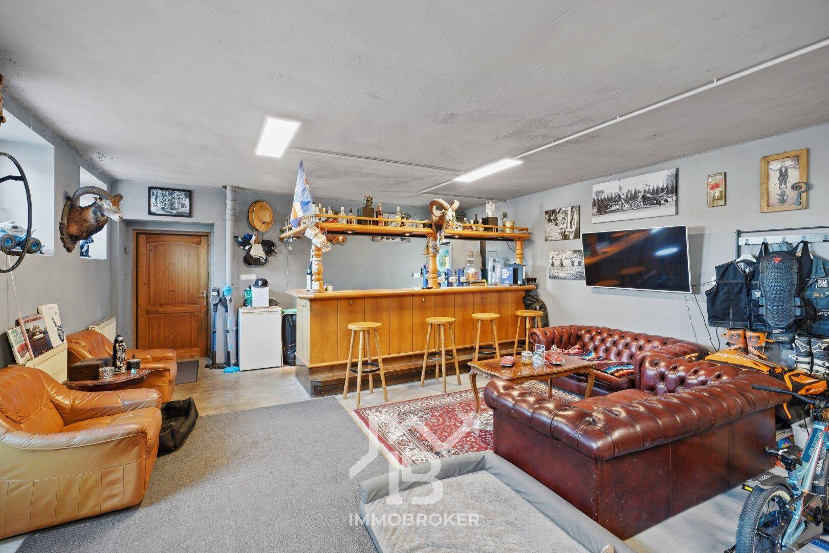 Gemütlicher Barbereich im Keller mit Ledersofas, Holztresen und Fernseher für gesellige Abende.