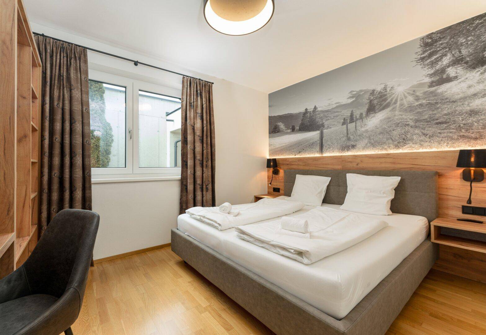 Gemütliches Schlafzimmer mit Doppelbett, Holzboden und Wandbild mit Berglandschaft.