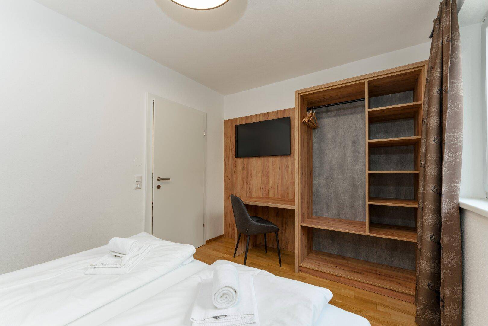 Schlafzimmer mit Doppelbett, integriertem Schreibtisch und offenem Kleiderschrank.