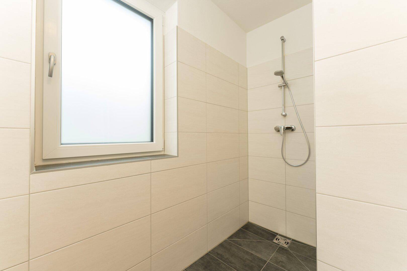 Geräumige Dusche im modernen Badezimmer mit Fliesen und Fenster für natürliche Belüftung.