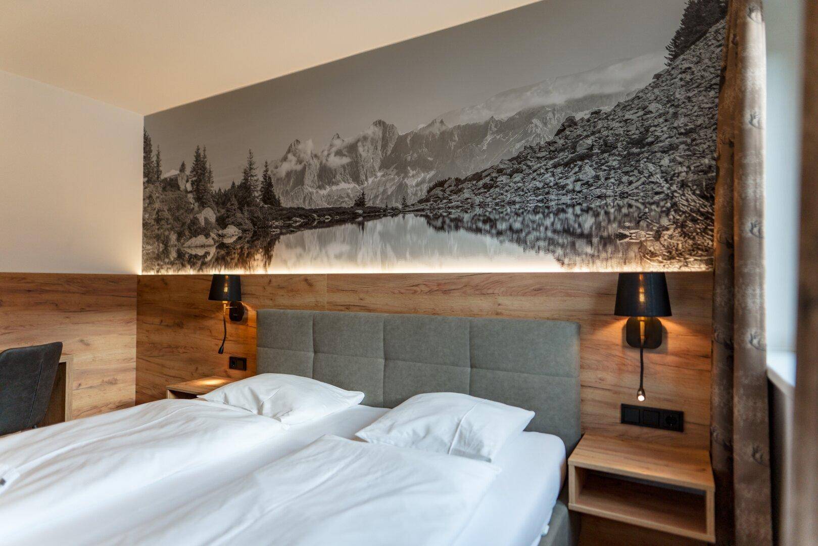 Detailansicht des Doppelbettes im Schlafzimmer mit alpiner Wanddekoration und Nachttischen.