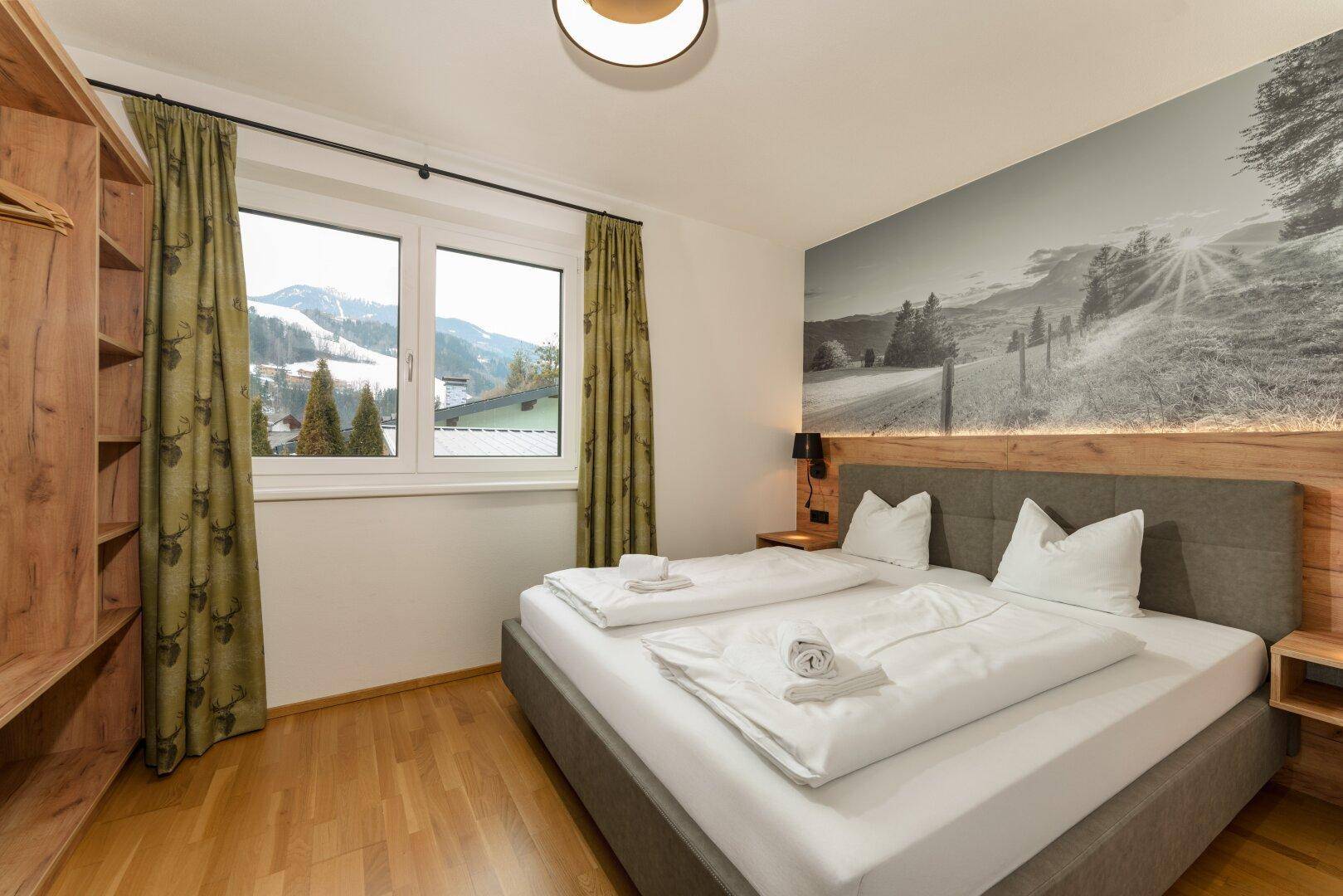 Helles Schlafzimmer mit Doppelbett, Holzboden und Fenster mit Blick auf die verschneiten Hügel.
