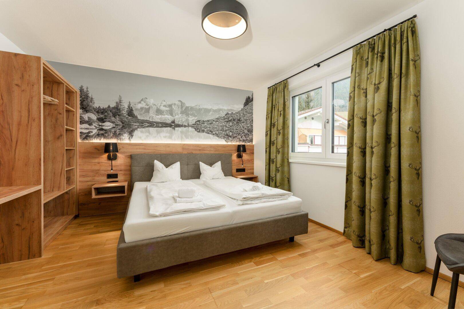 Gemütliches Schlafzimmer mit Doppelbett, Holzelementen und einer beeindruckenden Bergsee-Wandtapete.