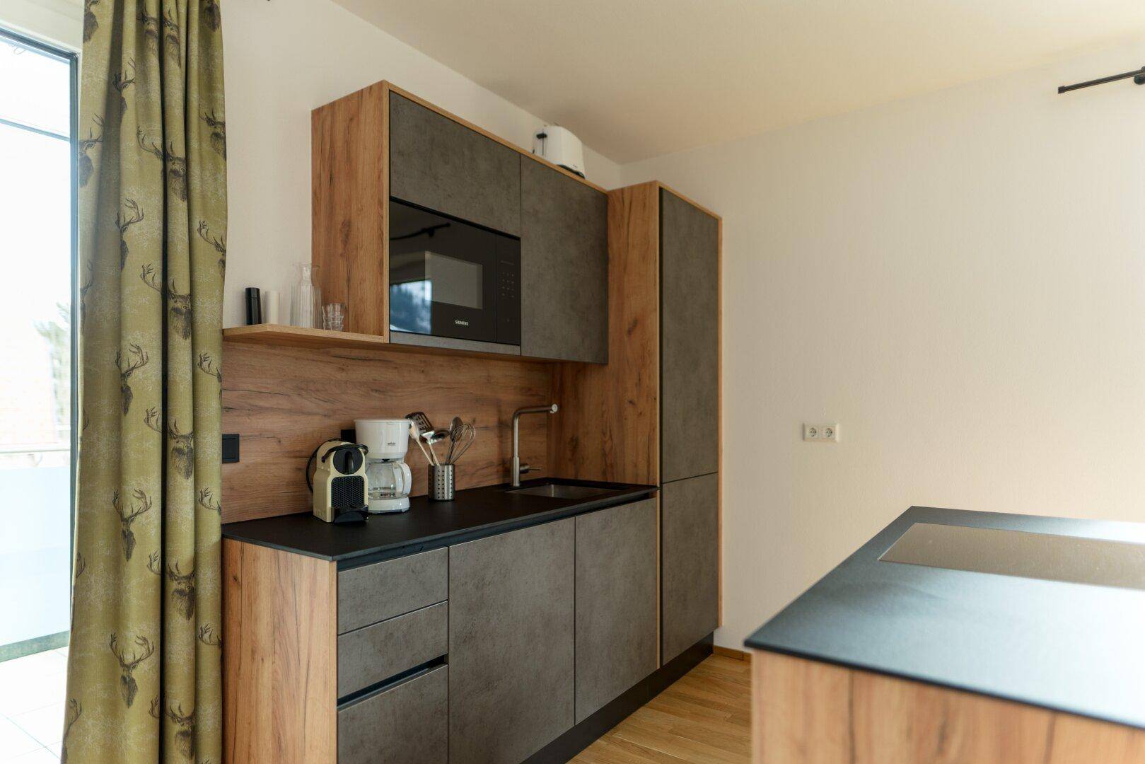 Detailansicht der modernen Küche mit Spülbecken, Mikrowelle und Kühlschrank, in Holz- und Steindesign.