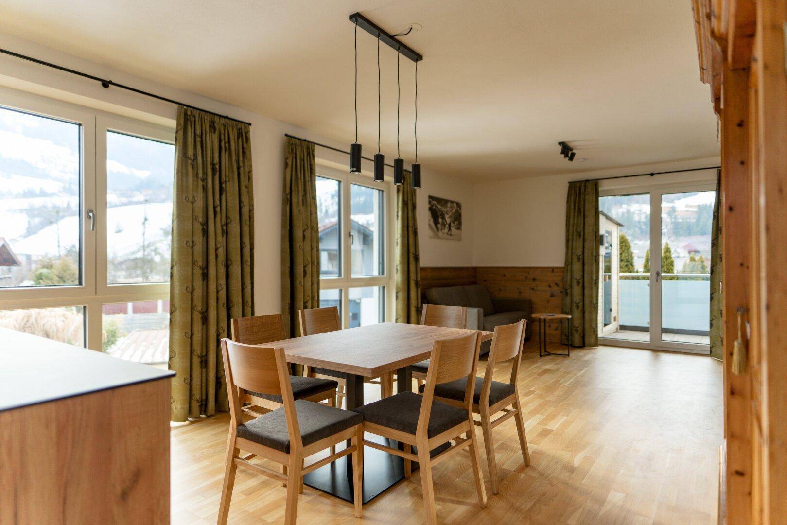 Heller Essbereich mit Holztisch und Stühlen, umgeben von großen Fenstern mit weitem Blick auf die Natur.