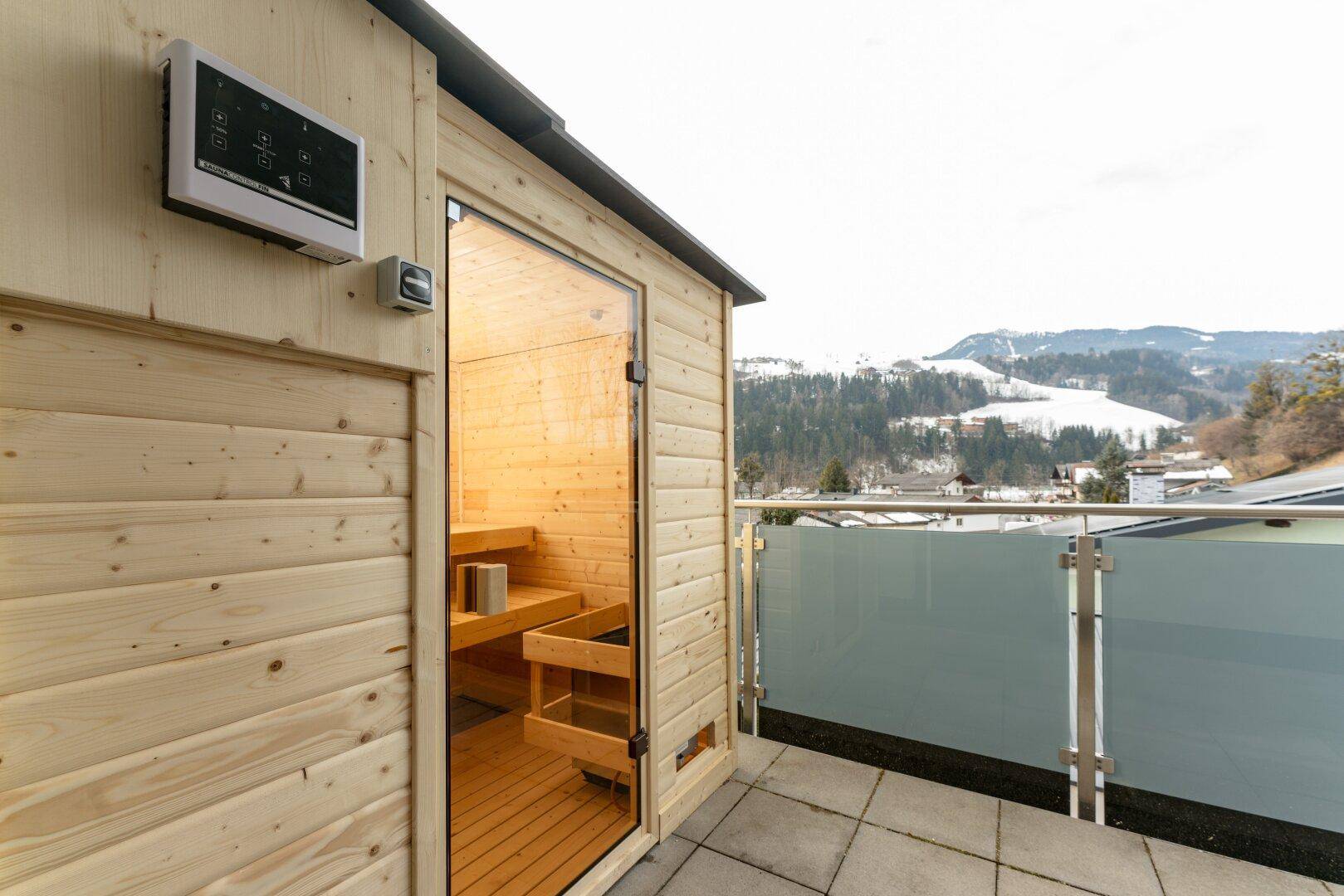 Private Außensauna auf dem Balkon mit Panoramablick auf die verschneiten Berge.