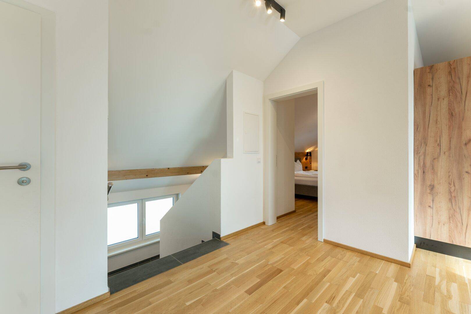 Geräumiger Flur mit Holzboden, Zugang zu den Zimmern und Blick auf die Treppe.