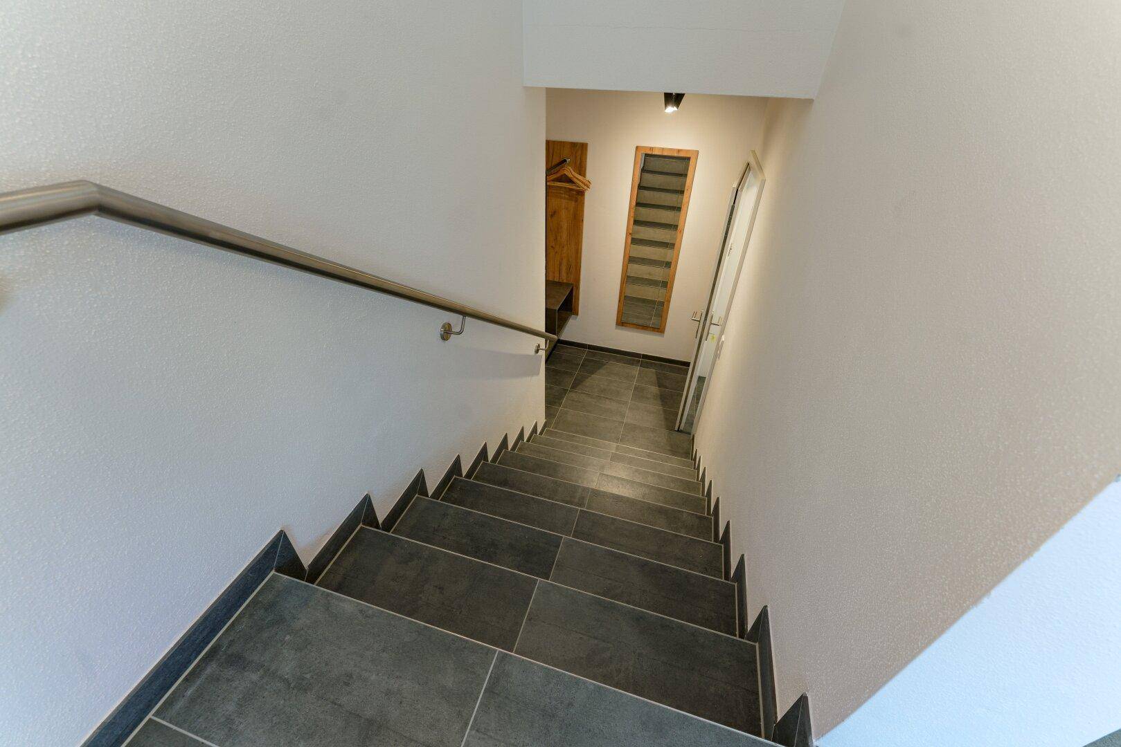 Moderne Treppe mit Fliesenbelag und stabilem Handlauf, führt in die untere Etage.