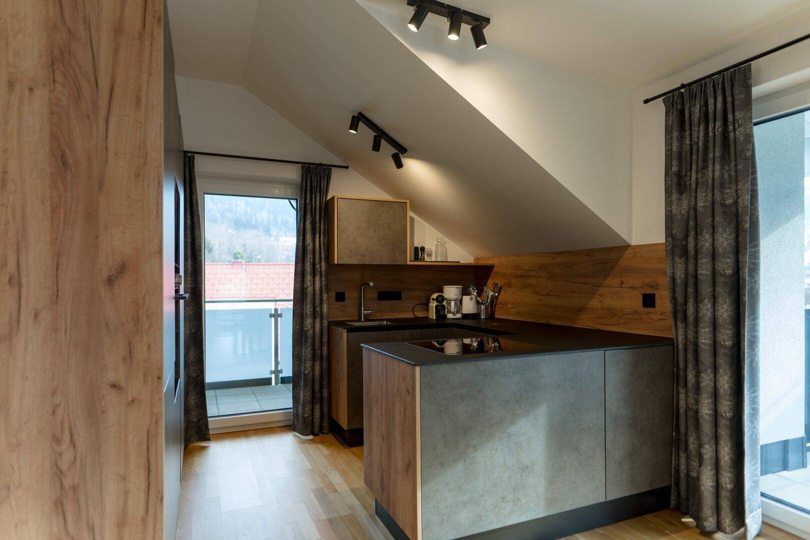 Moderne Einbauküche mit dunklen Arbeitsplatten, Holzelementen und Balkonzugang mit Bergblick.