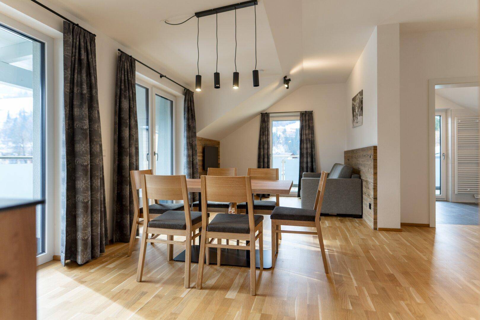 Gemütlicher Essbereich mit Holztisch und Stühlen, offen zum Wohnbereich und mit Balkonzugang.