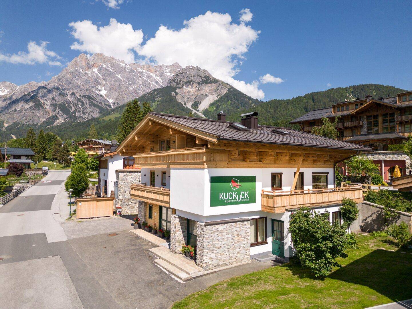 Traditionelles Alpenhaus mit Holzbalkonen und Steinakzenten vor majestätischer Bergkulisse.