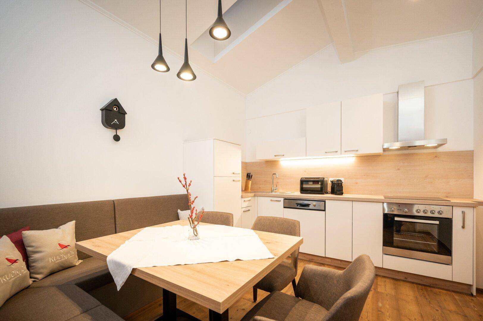 Lichtdurchflutete Küche mit Essbank, modernen Geräten und Holzboden in hellem Design.