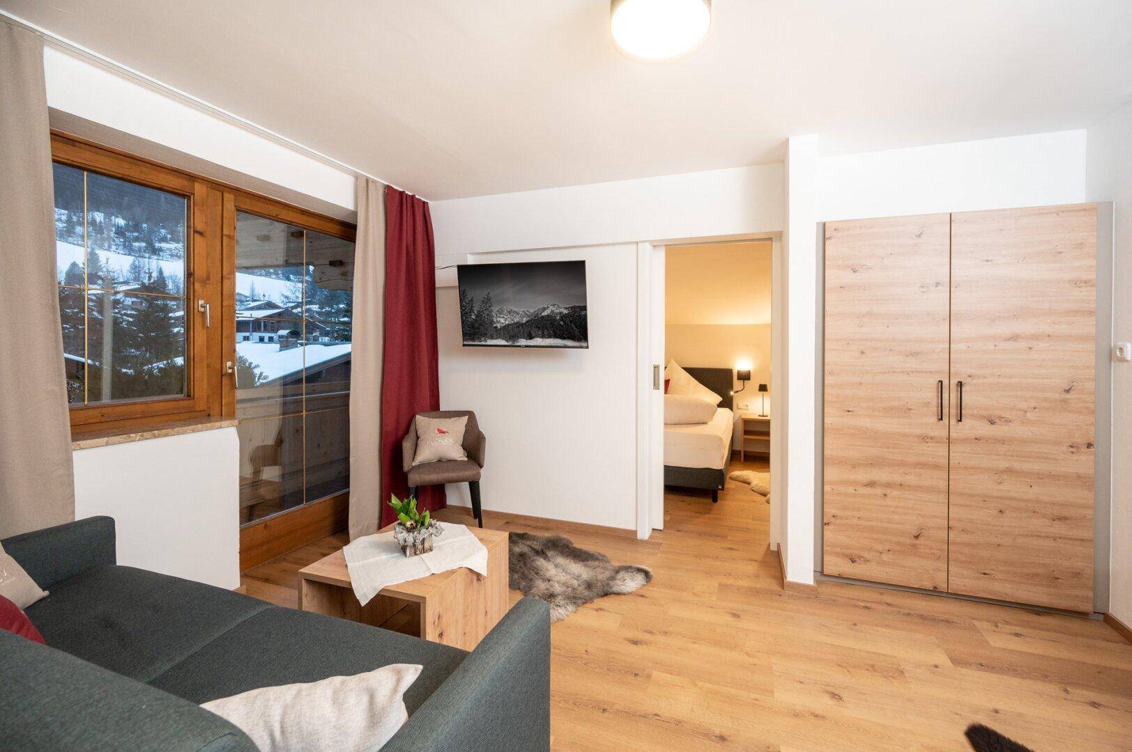 Wohnbereich mit Sofa, Fernseher und Zugang zu einem Schlafzimmer, ausgestattet mit Holzboden.