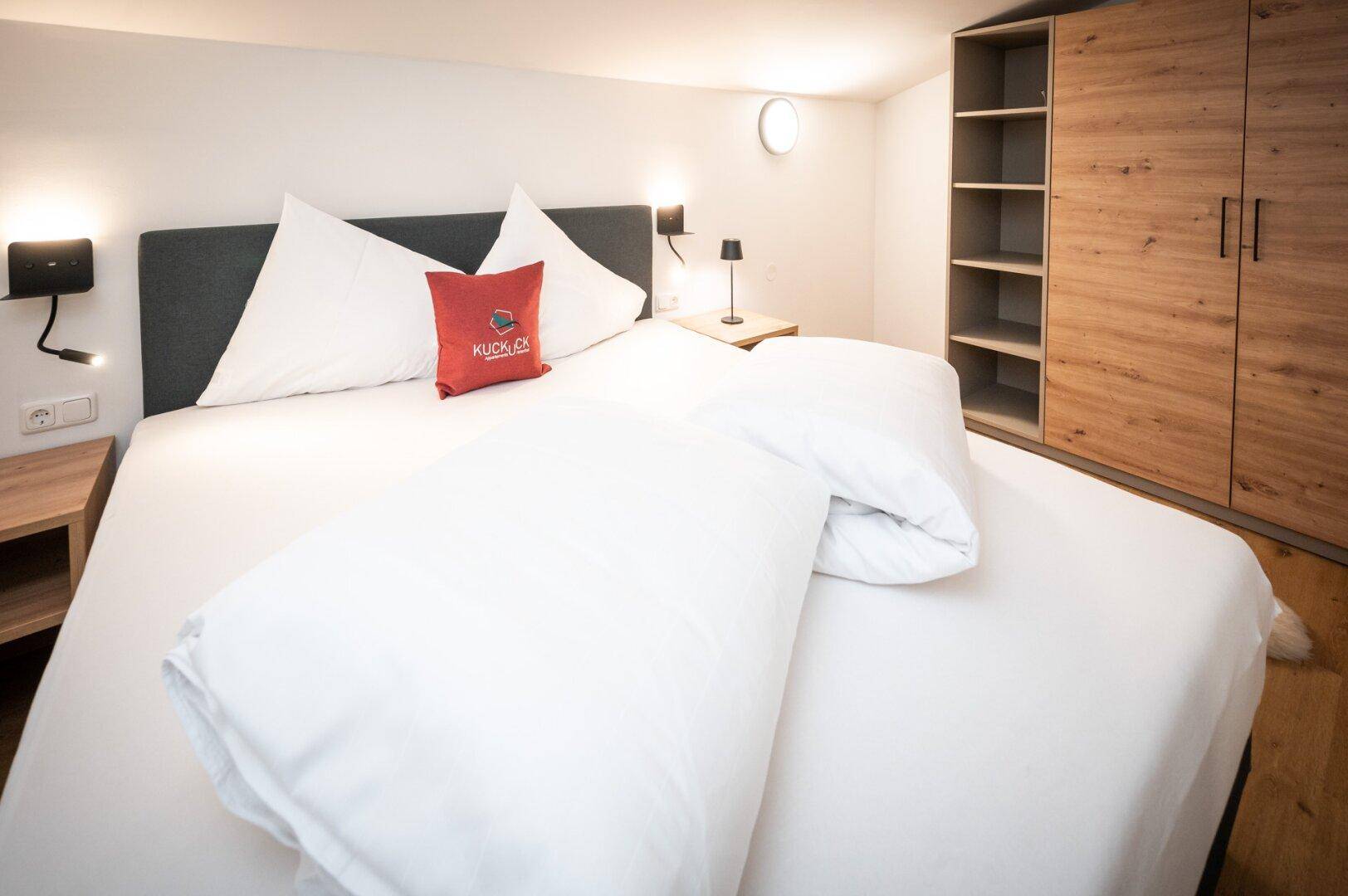 Helles Schlafzimmer mit Doppelbett, Holzboden und integriertem Kleiderschrank in modernem Stil.