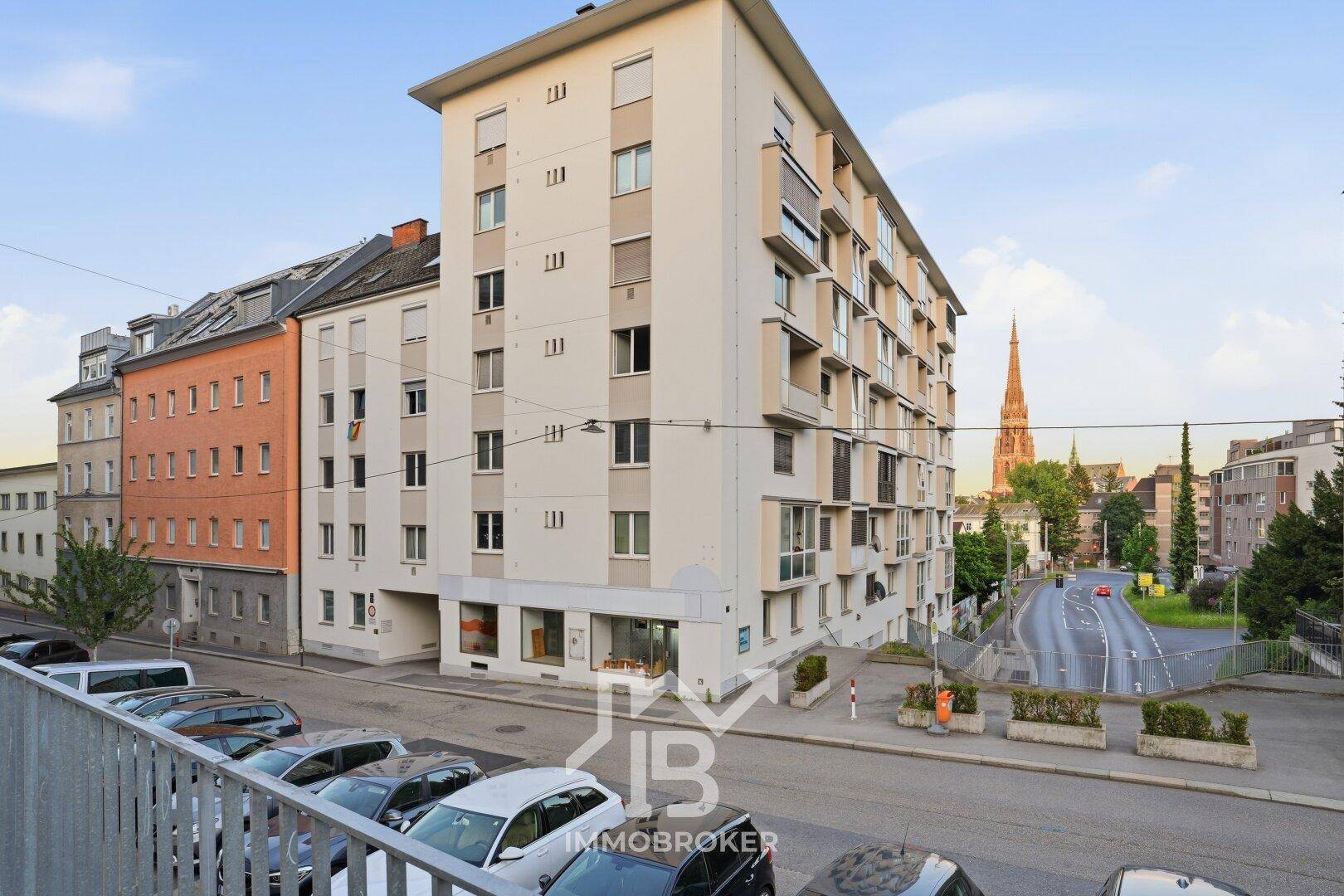 Mehrstöckiges Wohngebäude in städtischer Umgebung mit Parkplätzen davor.