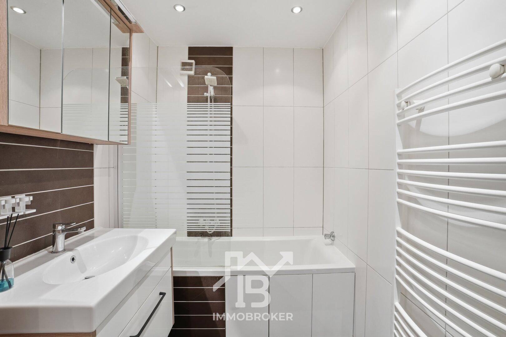 Helles Badezimmer mit Badewanne, Duschbereich und praktischem Handtuchheizkörper.