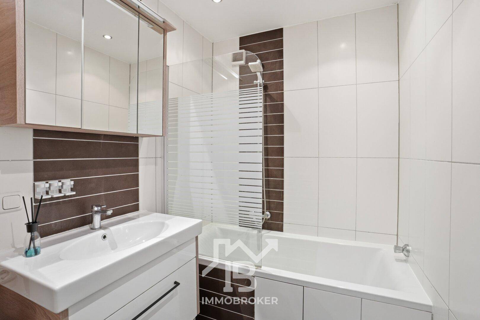 Modernes Badezimmer mit Badewanne, Dusche und eleganten braun-weißen Fliesen.