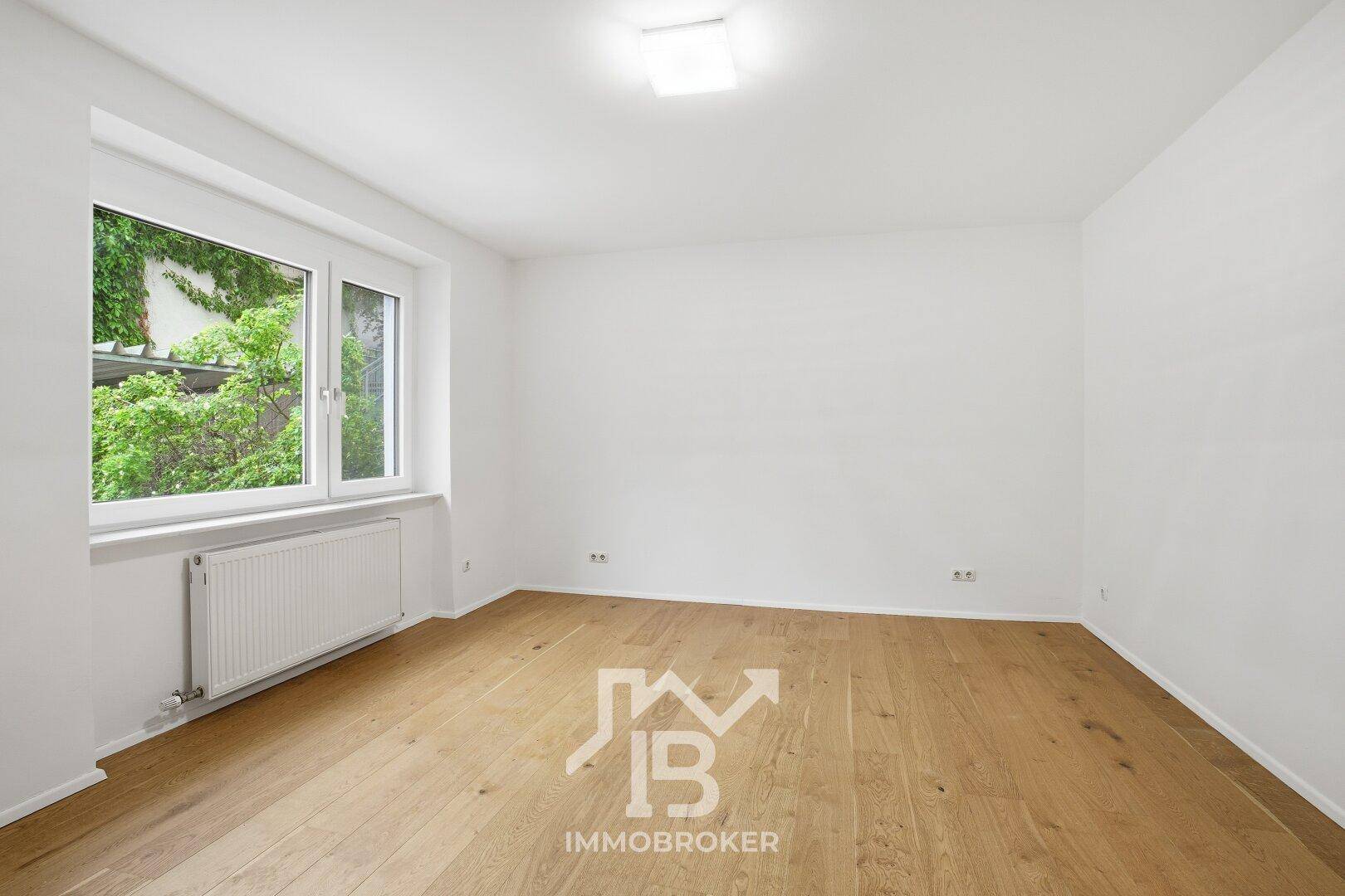 Heller Raum mit Holzfußboden und großem Fenster, das eine grüne Aussicht bietet.