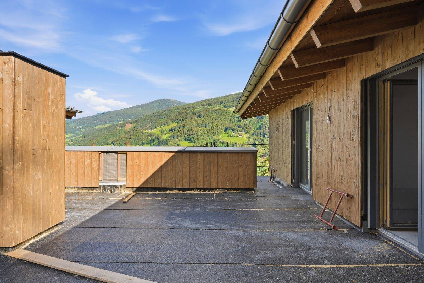 Unfertige Dachterrasse mit weitem Blick auf die grüne Berglandschaft unter blauem Himmel.