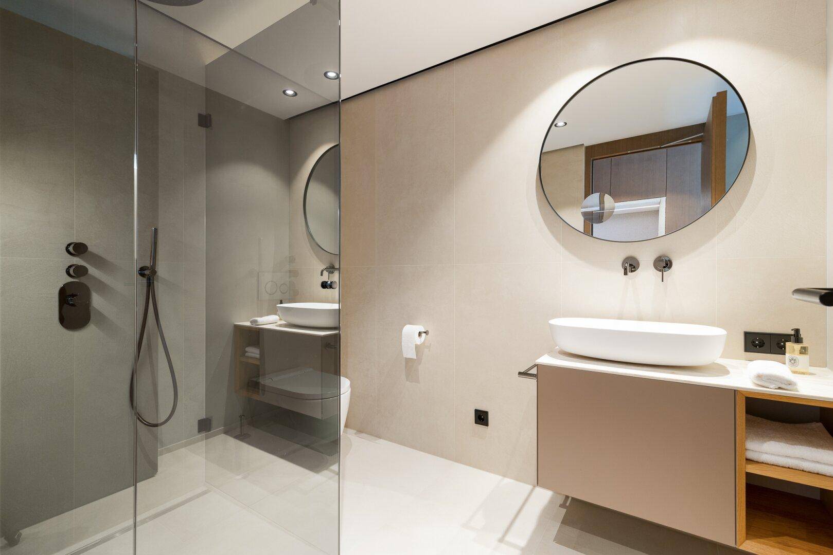 Modernes Badezimmer mit begehbarer Dusche, runden Spiegeln und eleganten schwarzen Armaturen.