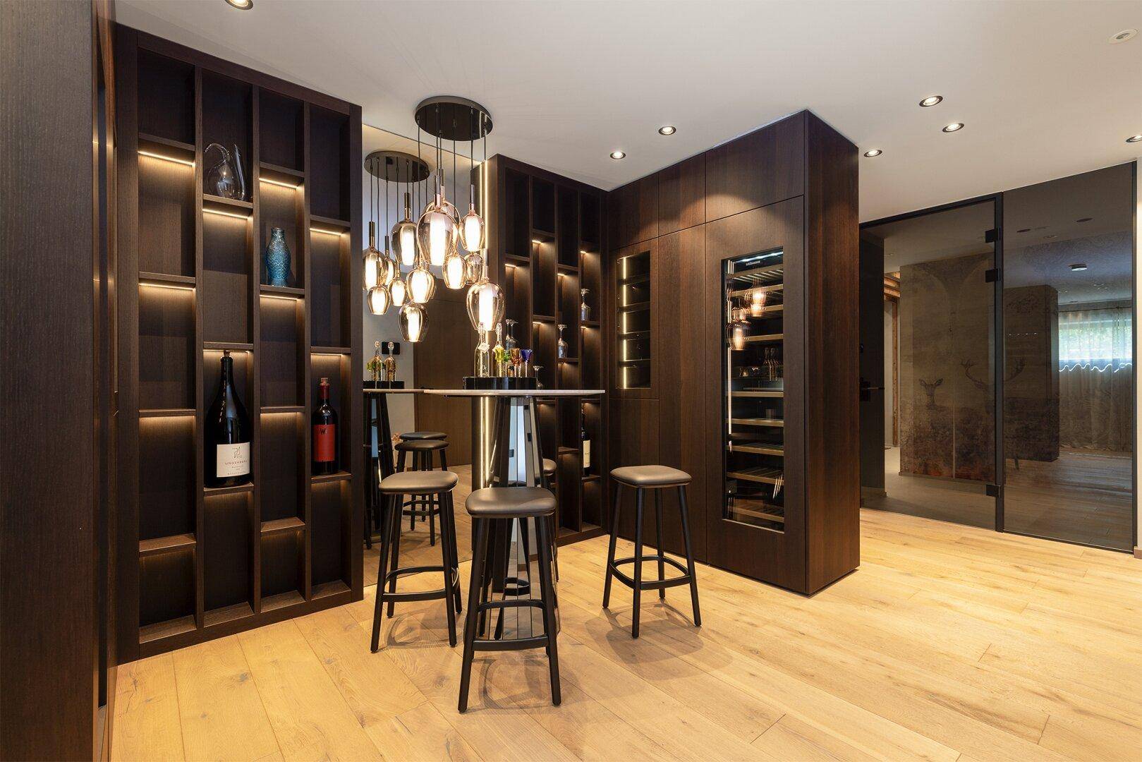 Exklusiver Weinkeller mit Bar, beleuchteten Regalen und modernen Pendelleuchten.