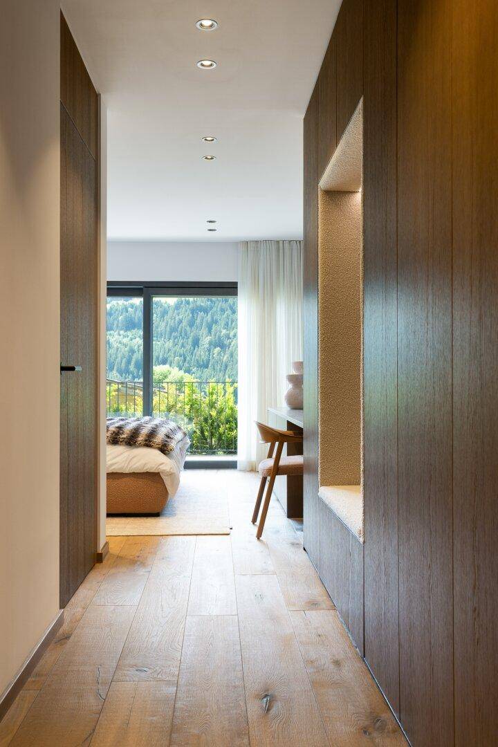 Moderner Flur mit Holzboden und Blick in ein helles Schlafzimmer mit Bergblick durch die Tür.