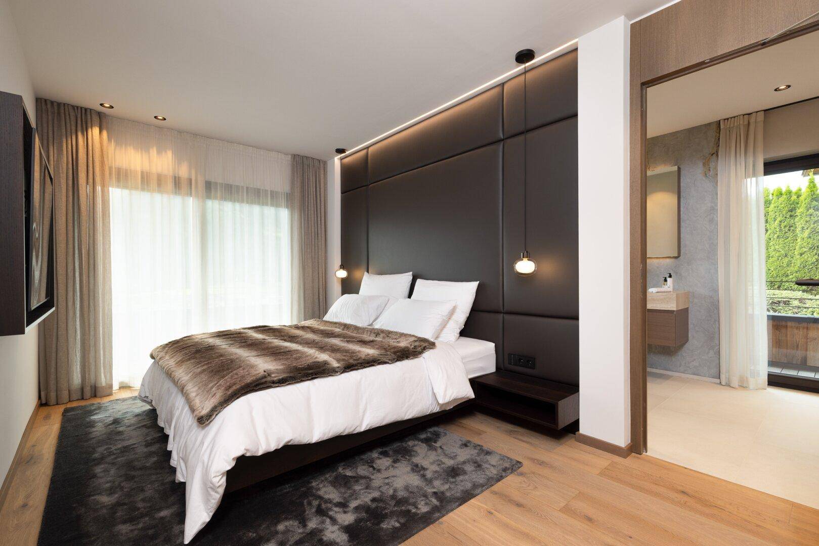 Geräumiges Schlafzimmer mit gepolstertem Kopfteil, Holzboden und Zugang zu einem Balkon.