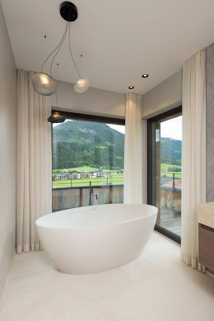 Helles Badezimmer mit freistehender Badewanne und großen Fenstern, die einen weiten Bergblick bieten.