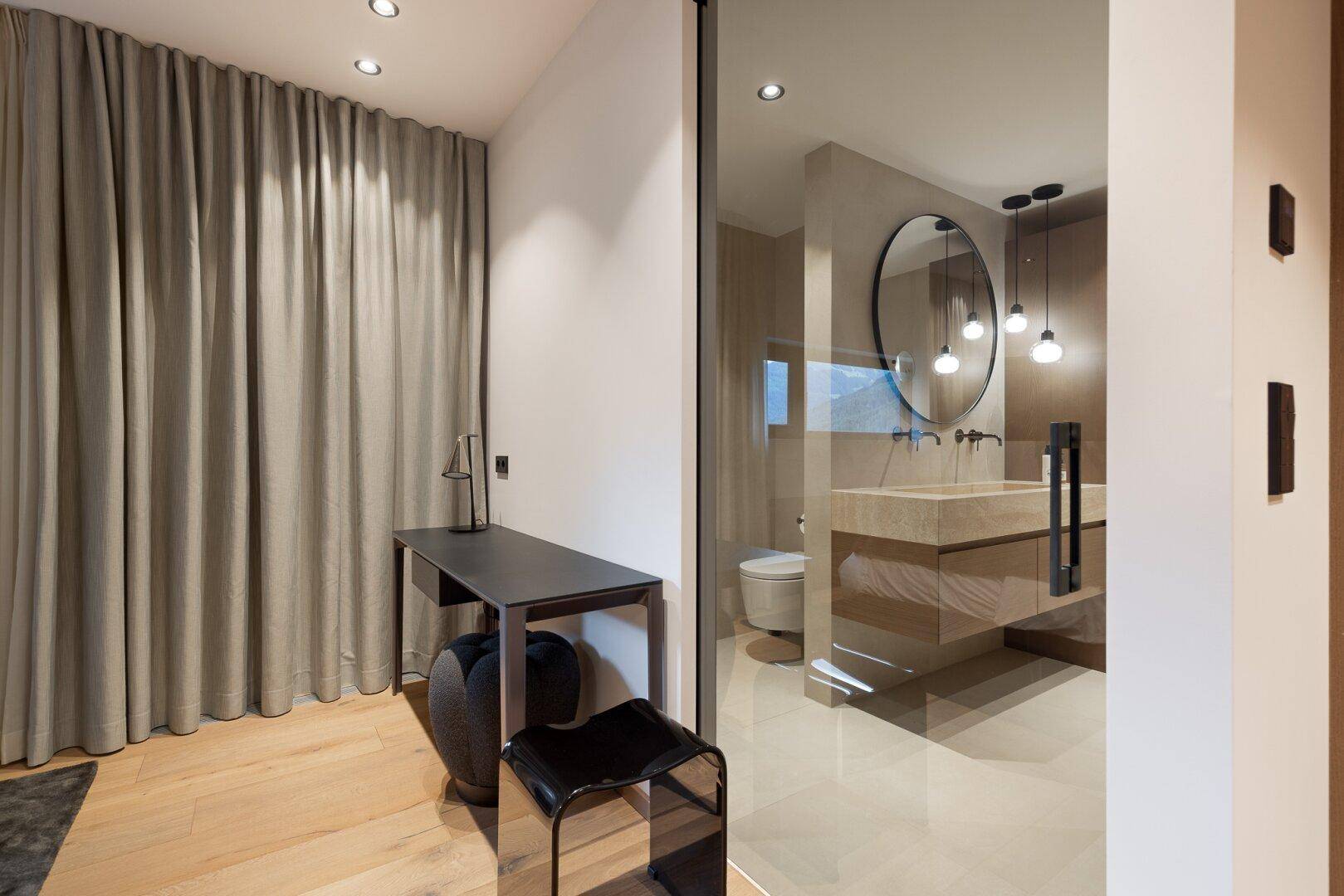 Schlafzimmer mit Holzboden und Blick durch eine Glaswand in ein modernes Ensuite-Badezimmer.