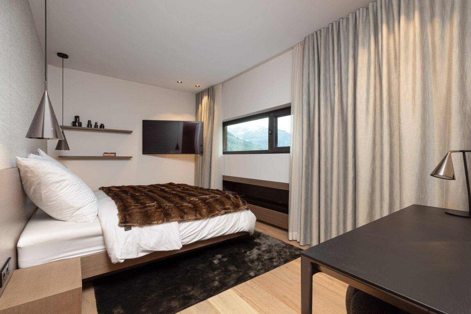 Gemütliches Schlafzimmer mit Einzelbett, Fernseher und kleinem Fenster mit Bergblick.