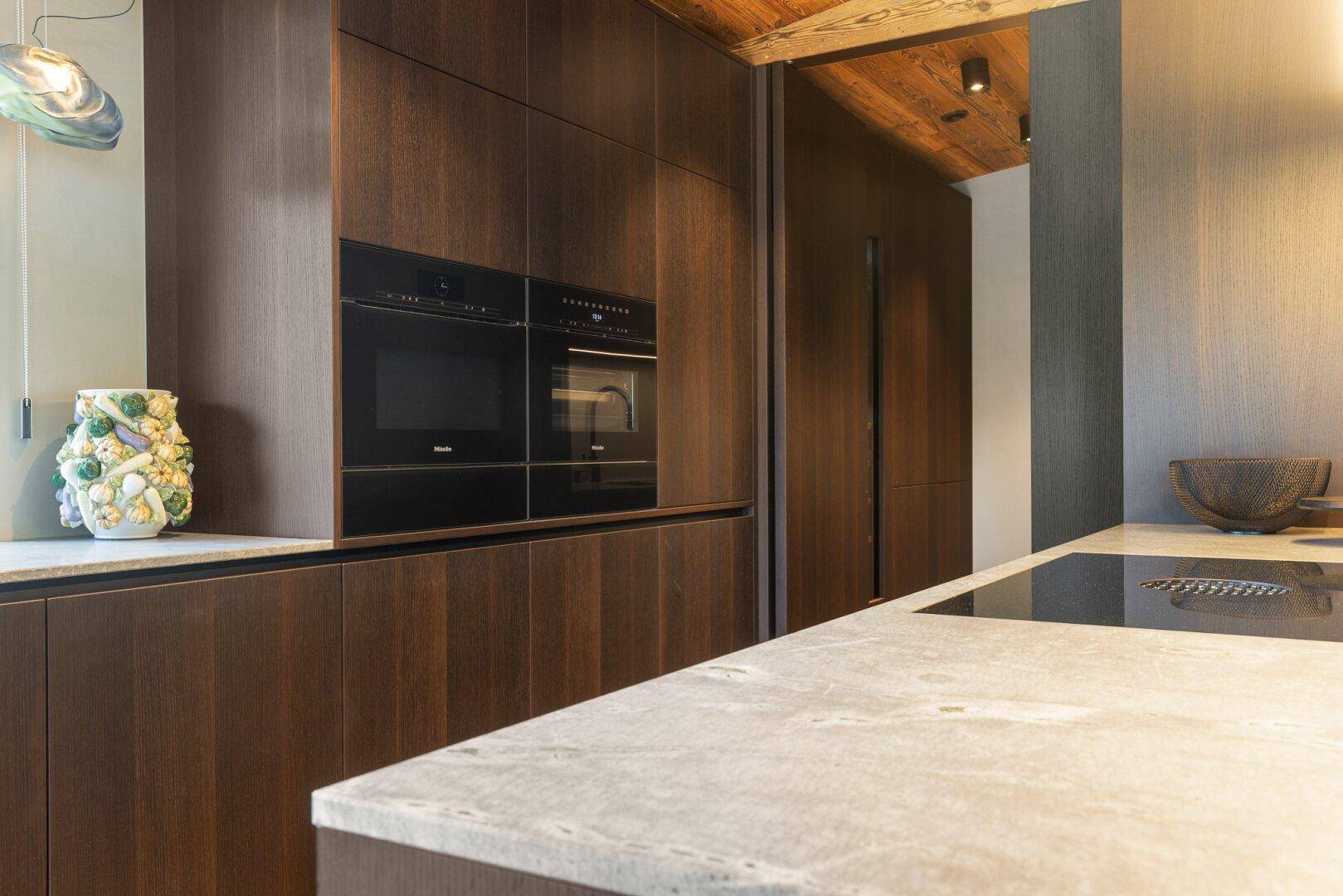 Hochwertige Einbauküche mit dunklen Holzfronten, integrierten Geräten und Stein-Arbeitsplatte.