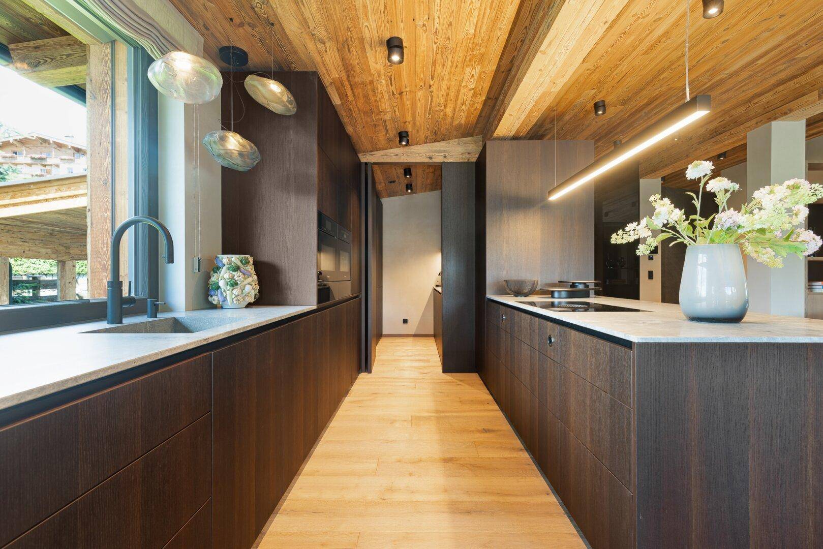 Elegante Küche mit dunklen Holzschränken, Kücheninsel und modernen Geräten.