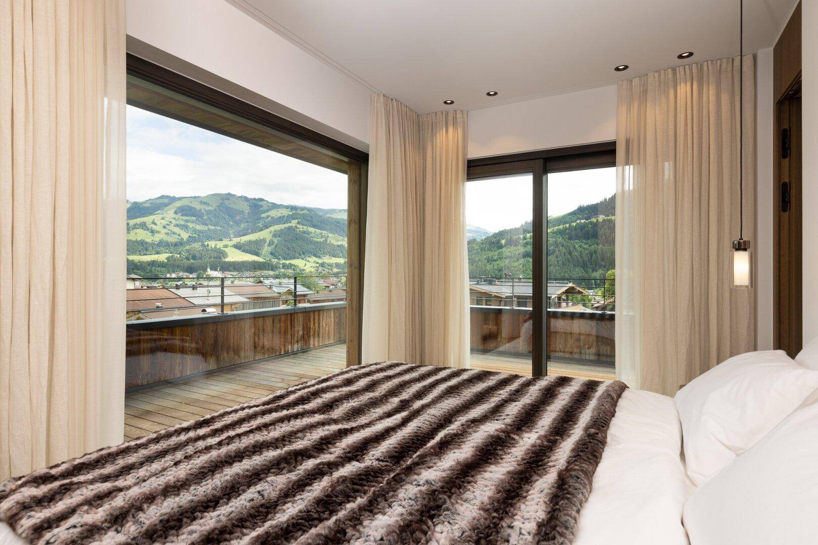 Helles Schlafzimmer mit großem Bett, Balkonzugang und weitem Bergblick.