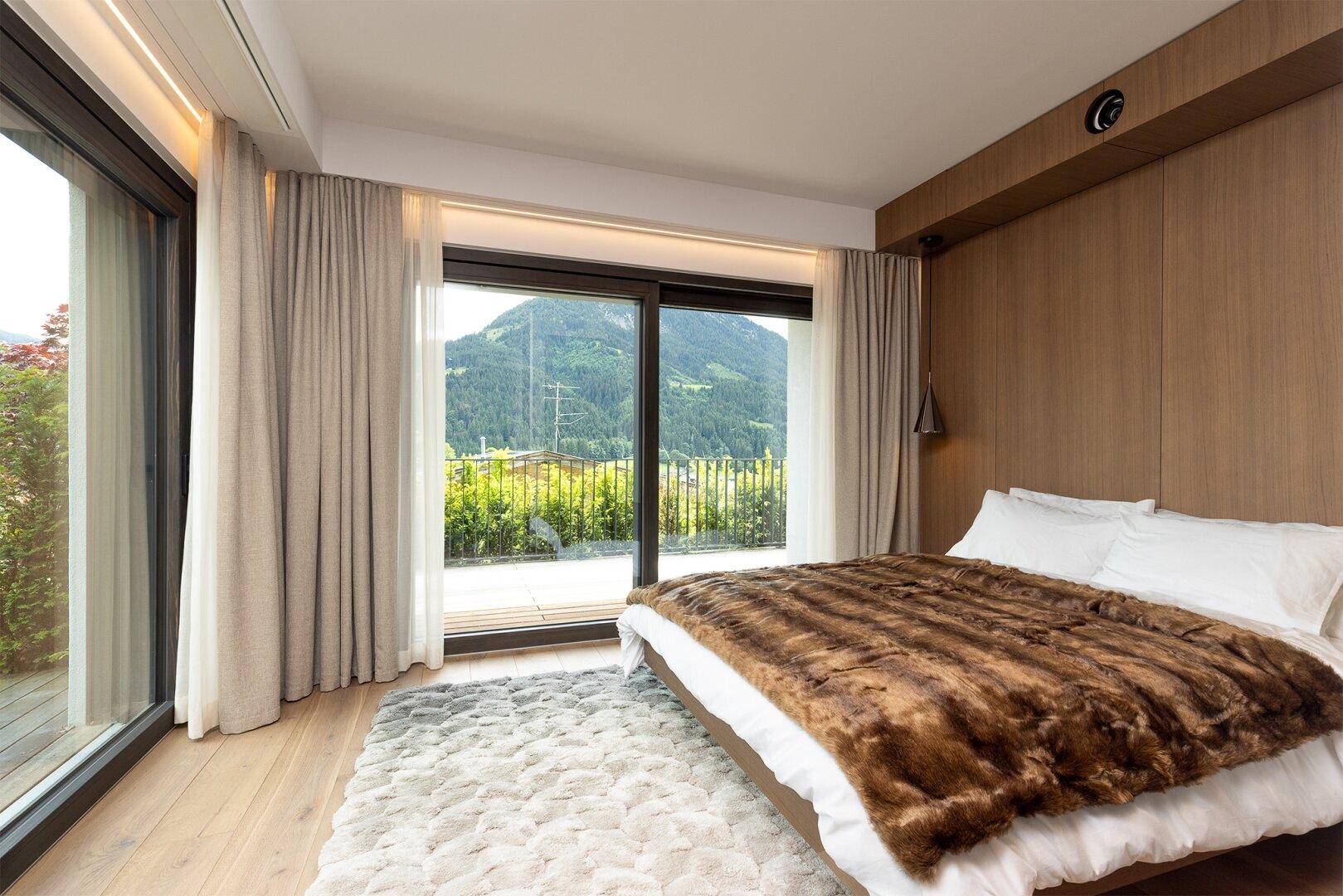 Helles Schlafzimmer mit Holzboden, großen Fenstern und Bergblick, ausgestattet mit einem flauschigen Teppich.