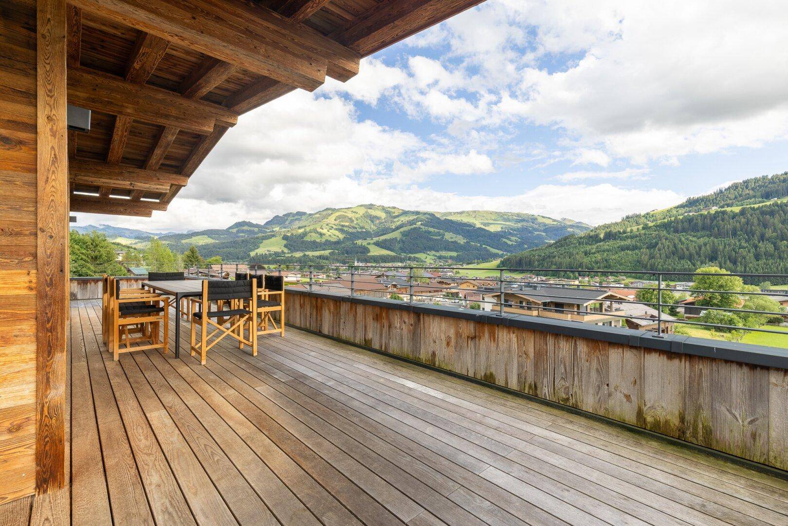 Große Holzterrasse mit Esstisch und Stühlen, umgeben von einer malerischen Berglandschaft.