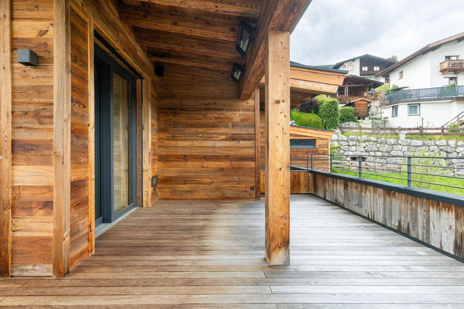 Überdachte Holzterrasse mit rustikalem Charme und Blick auf die grüne Umgebung.