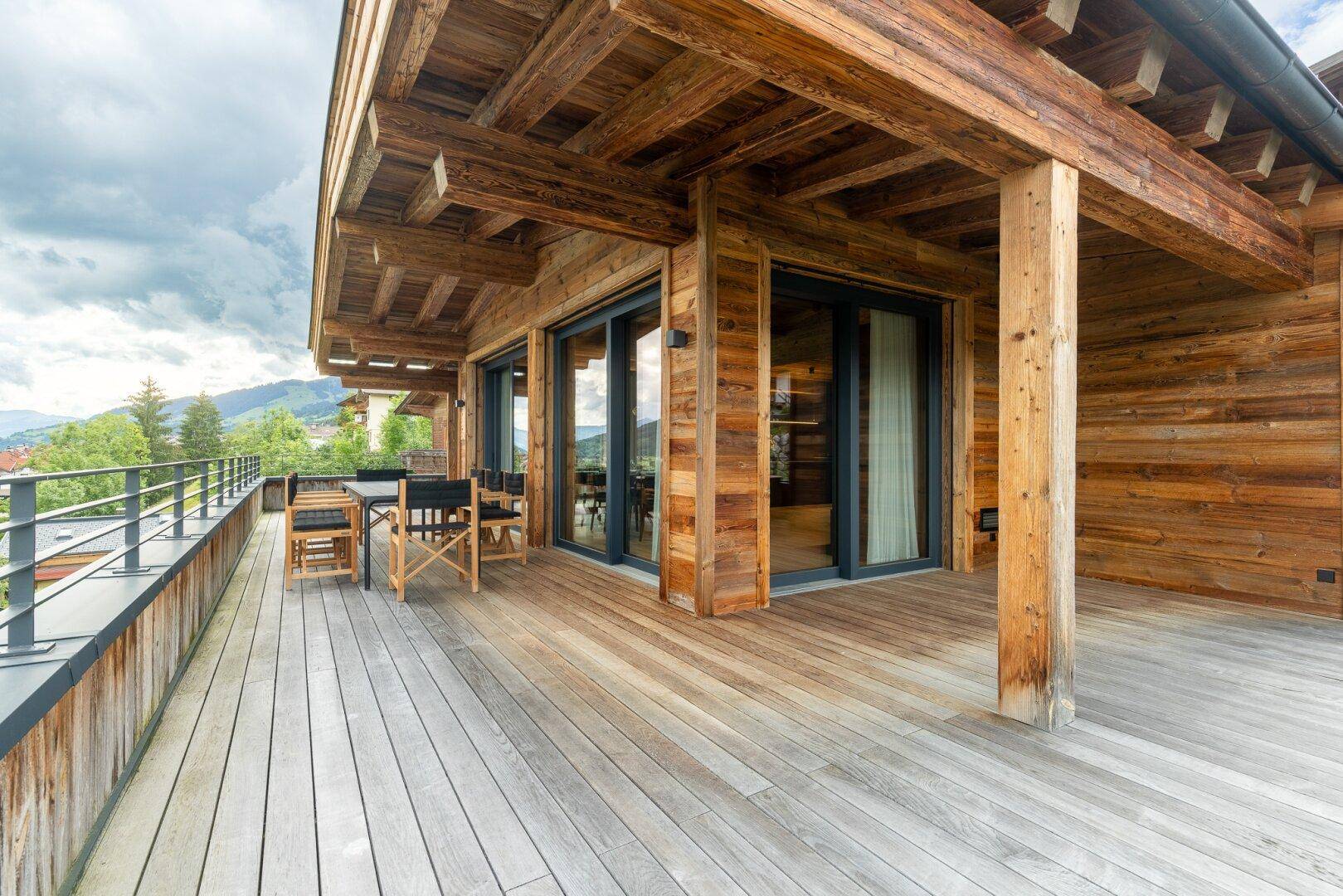 Weitläufige Holzterrasse mit Essbereich und Zugang zu Innenräumen, umgeben von Natur.