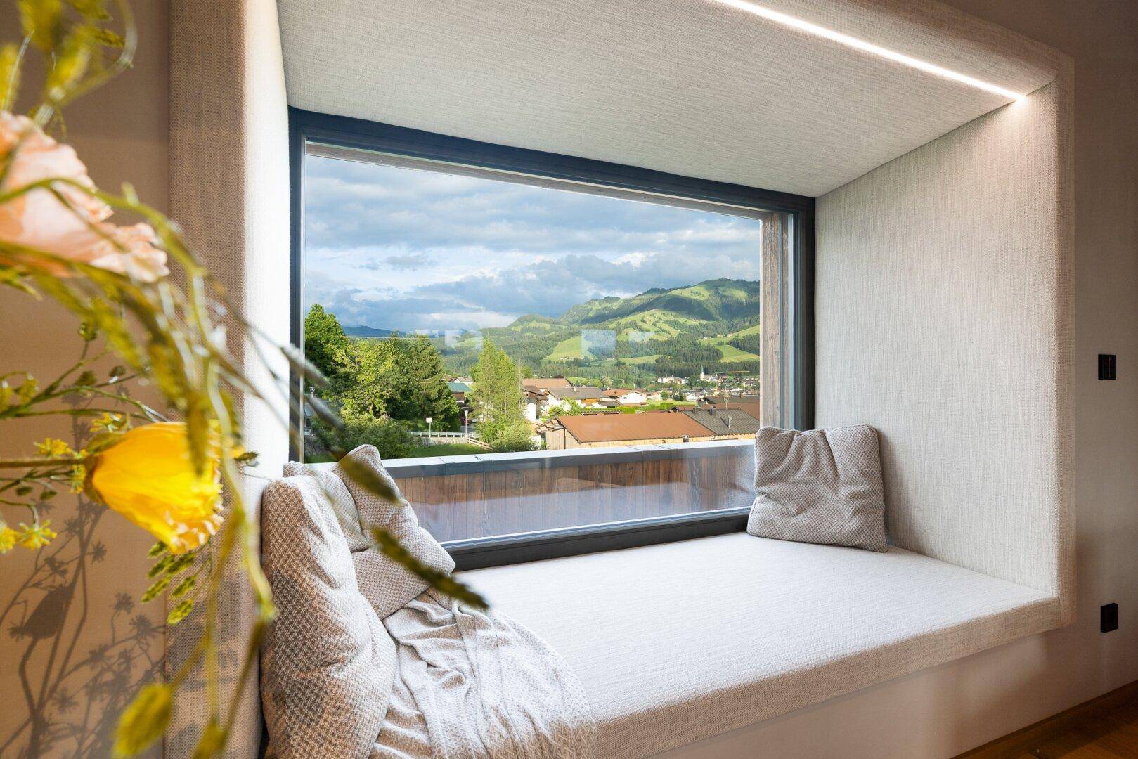 Einladender Fensterplatz mit Kissen und weitem Blick auf die umliegende Berglandschaft.